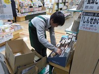 書架の前で屈んで品物の補充をする生徒
